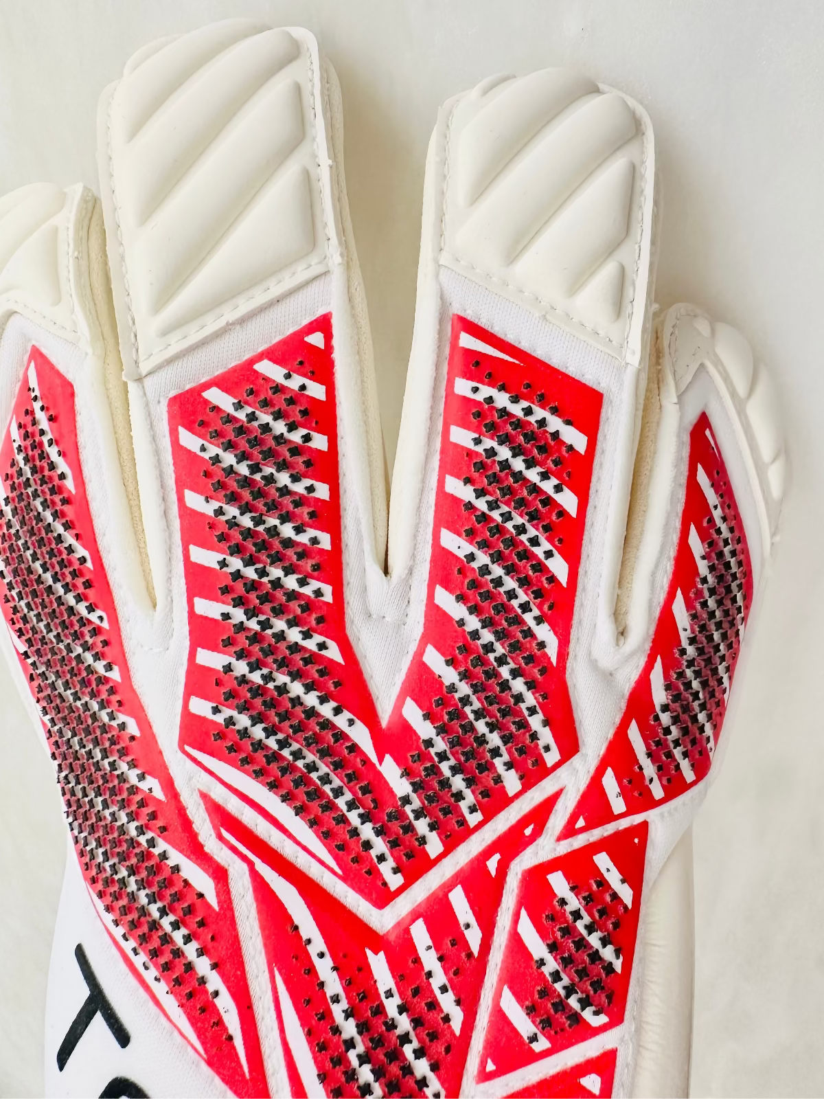 A close-up of a Tee3 goalkeeper glove showing the back of the hand with raised dotted punch pad details in a bright red colour and white padded finger sections 
