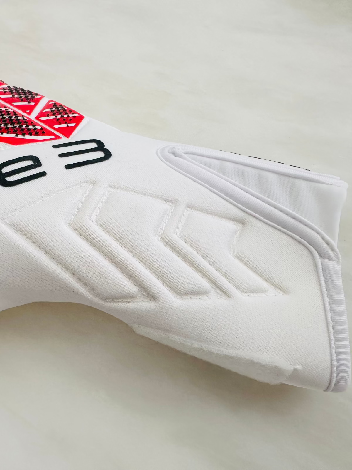 A close-up of a white TEE-3 professional goalkeeping brand wrist entry goalkeeper glove with red and white graphic accents, made from neoprene with specific accents and details. There is an easy entry at the beginning of the tunnel 
