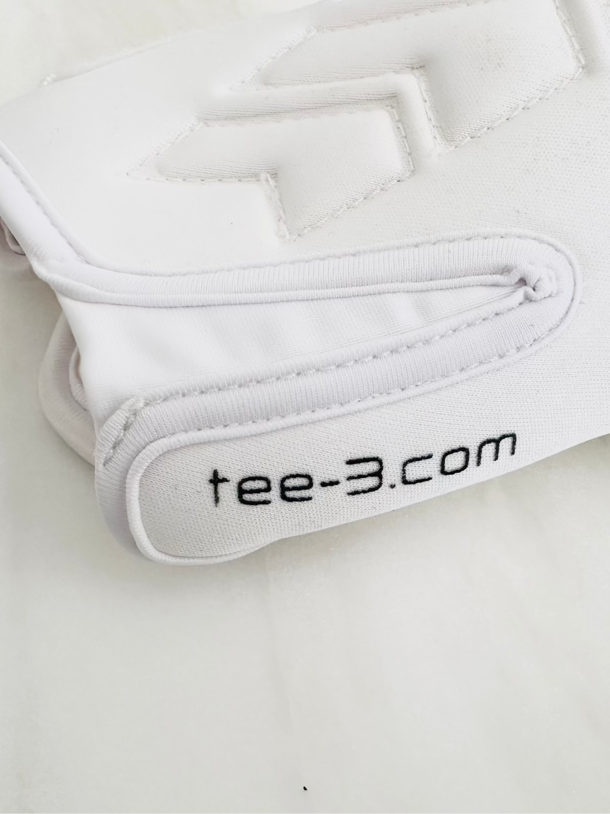 A close-up of a white TEE-3 professional goalkeeping brand wrist entry goalkeeper glove with the website address "www.tee-3.com" printed graphic accents, made from neoprene with specific accents and details. There is an easy entry at the beginning of the tunnel all set against a white background