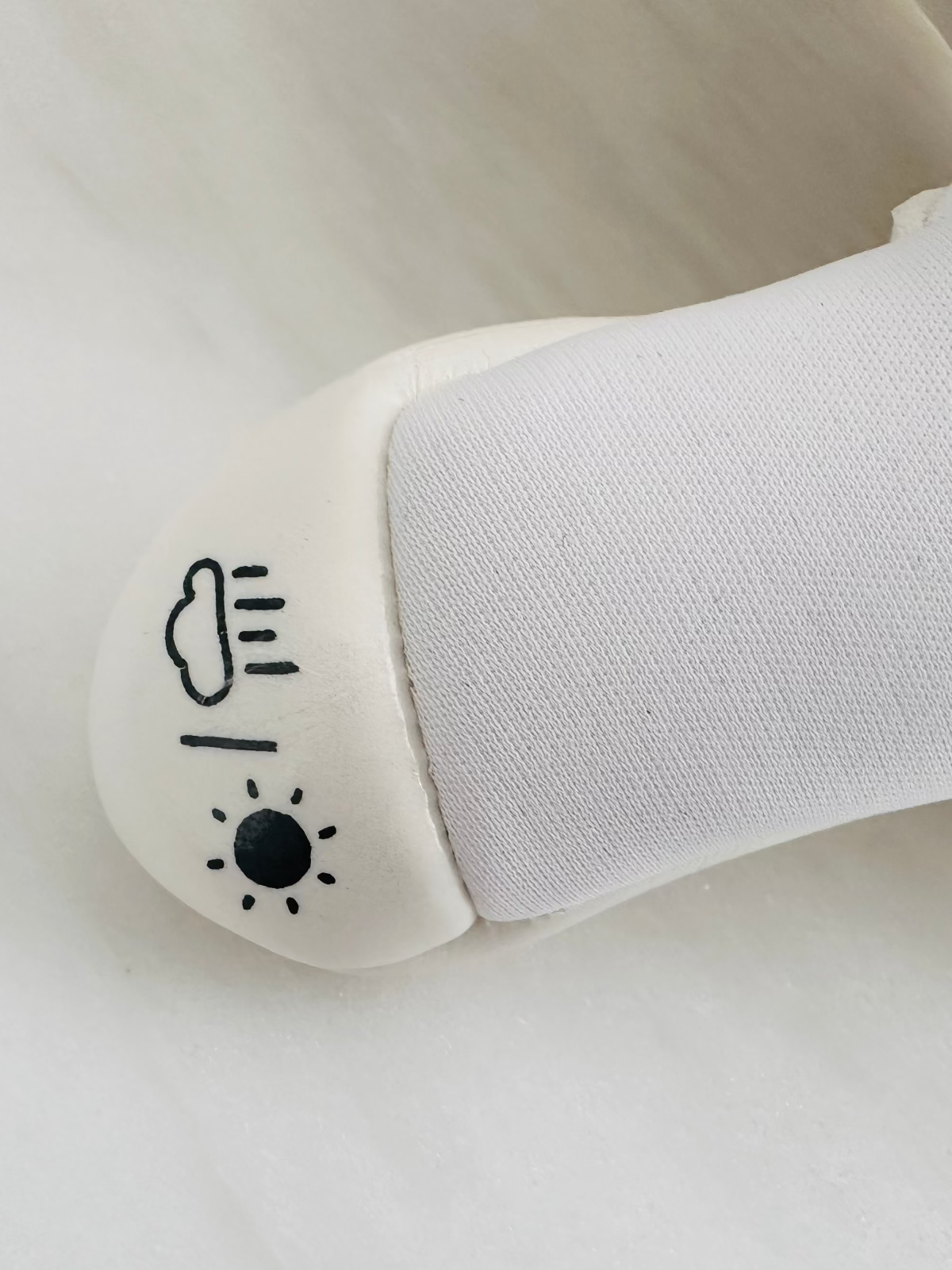 A close-up of a white TEE-3 professional goalkeeping brand wrapped thumb with the rain and sun icons printed showing that it can be used in wet weather and warm weather made from neoprene and white contact latex