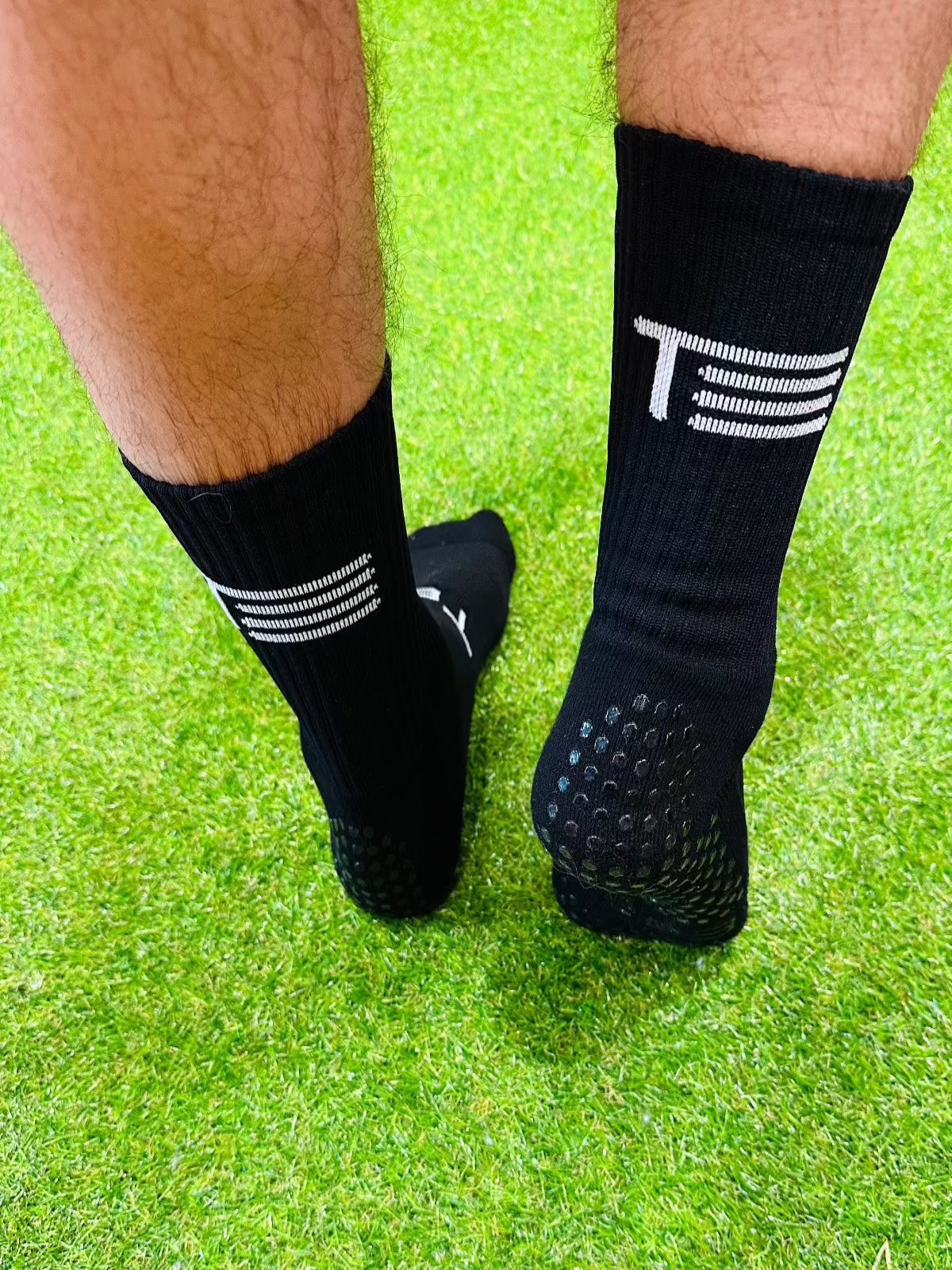 A pair of black Tee3 Goalkeeping sports grip socks with advanced grip technology, displayed on a grass surface.