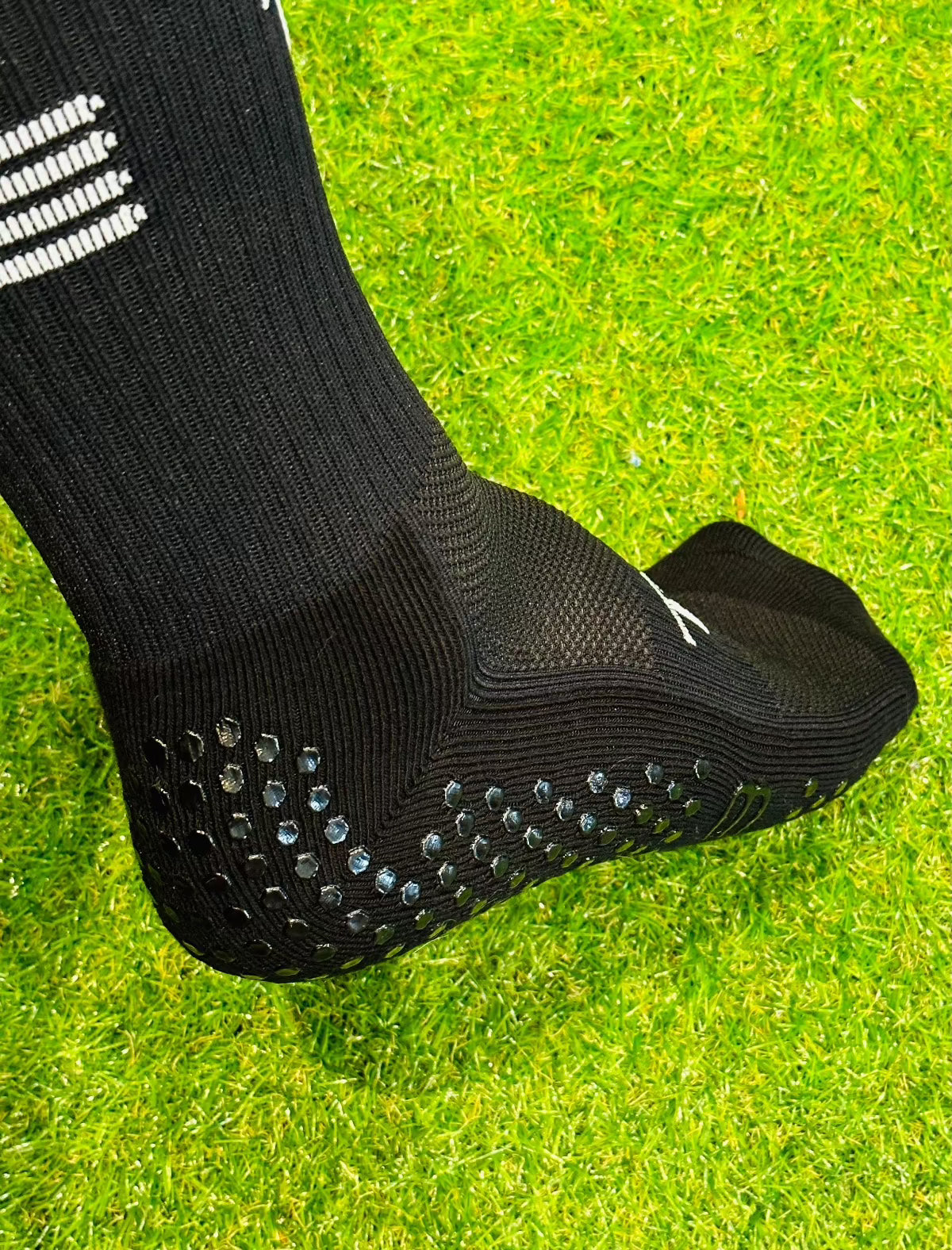 A pair of black Tee3 Goalkeeping sports grip socks with advanced grip technology, displayed on a grass surface.
