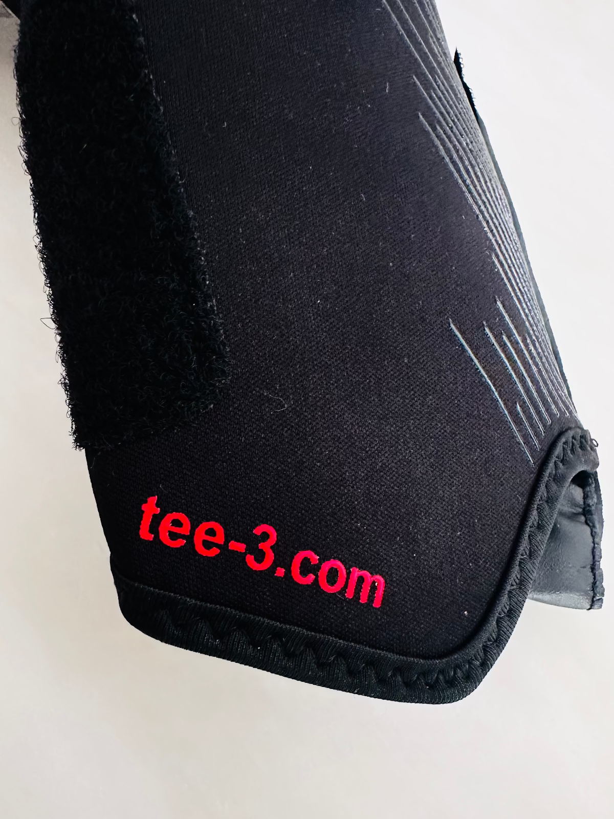 A close-up of a black TEE-3 professional goalkeeping brand wrist entry minimalist goalkeeper glove with pink and white graphic accents, made from neoprene with specific accents and details. The website address "www.tee-3.com" is printed at the beginning of the tunnel 