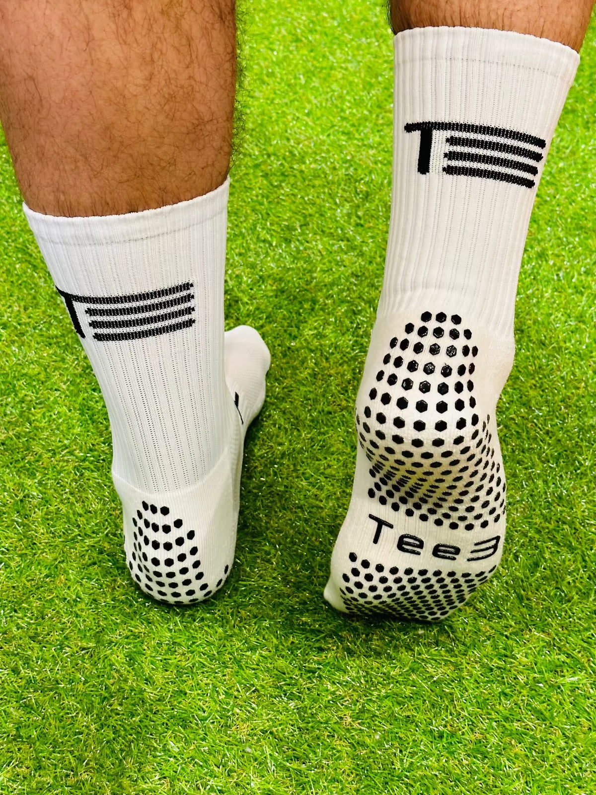 A pair of white high-performance grip socks with black details and the brand 'Tee3' displayed prominently on the side.