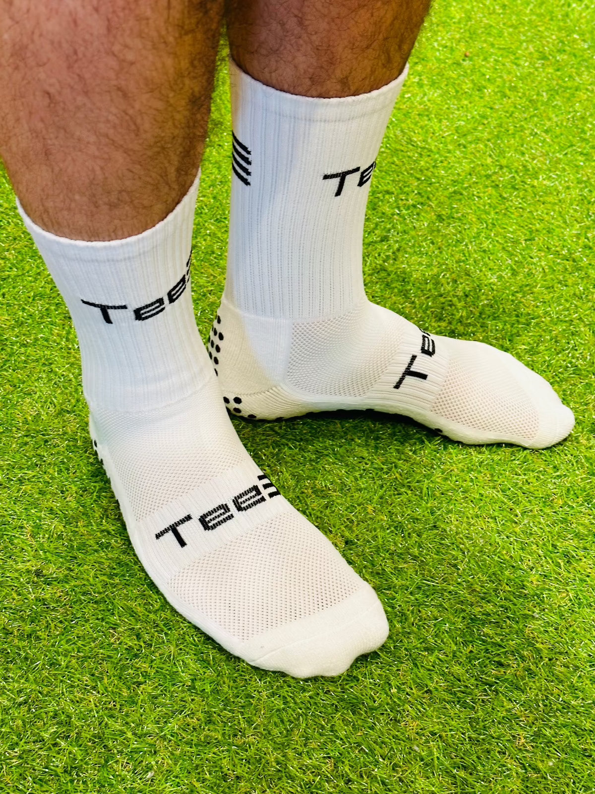 A pair of white high-performance grip socks with black details and the brand 'Tee3' displayed prominently on the side.