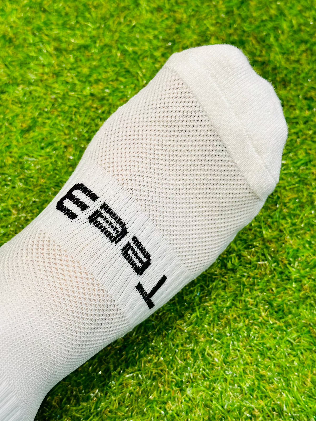A pair of white Tee3 Goalkeeping sports grip socks with advanced grip technology, displayed on a grass surface.
