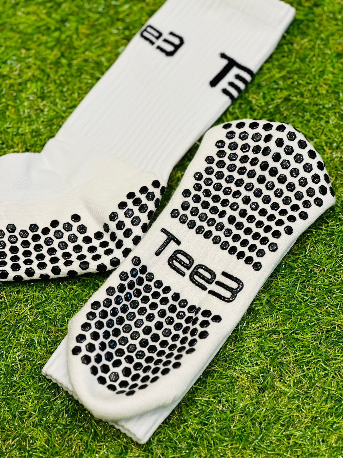 A pair of white high-performance grip socks with black details and the brand 'Tee3' displayed prominently on the side.
