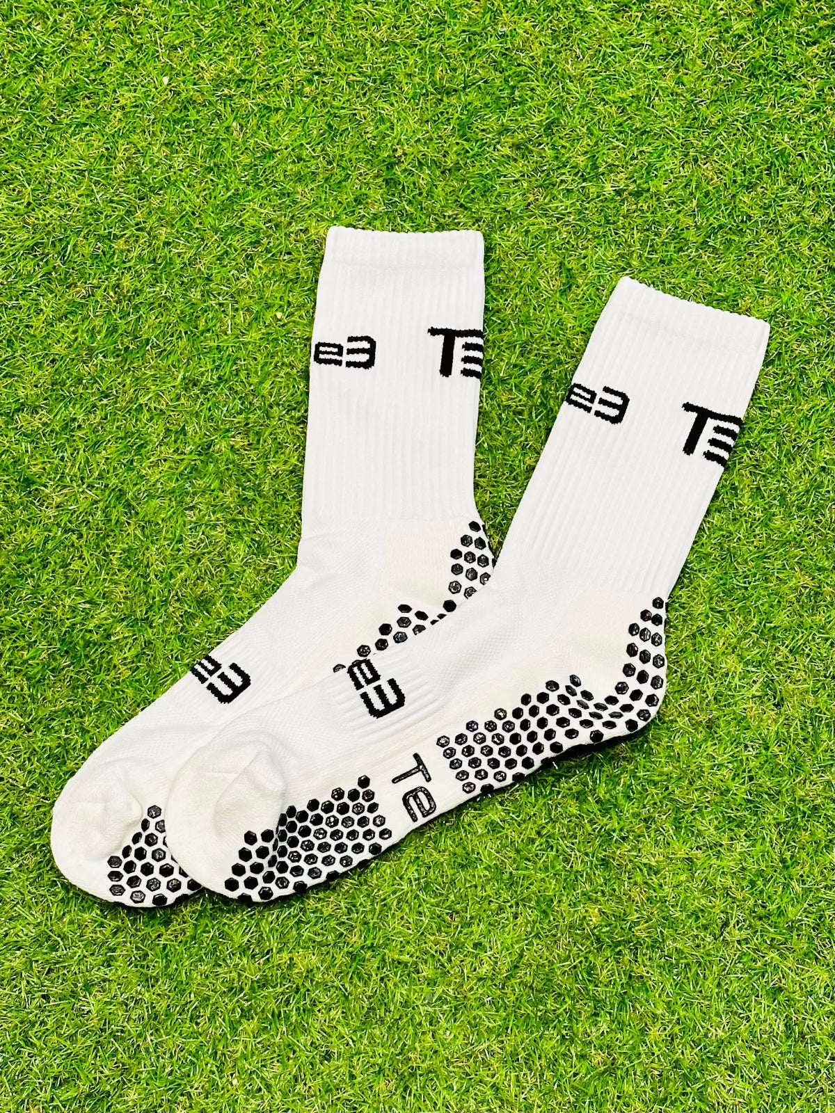A pair of white high-performance grip socks with black details and the brand 'Tee3' displayed prominently on the side.
