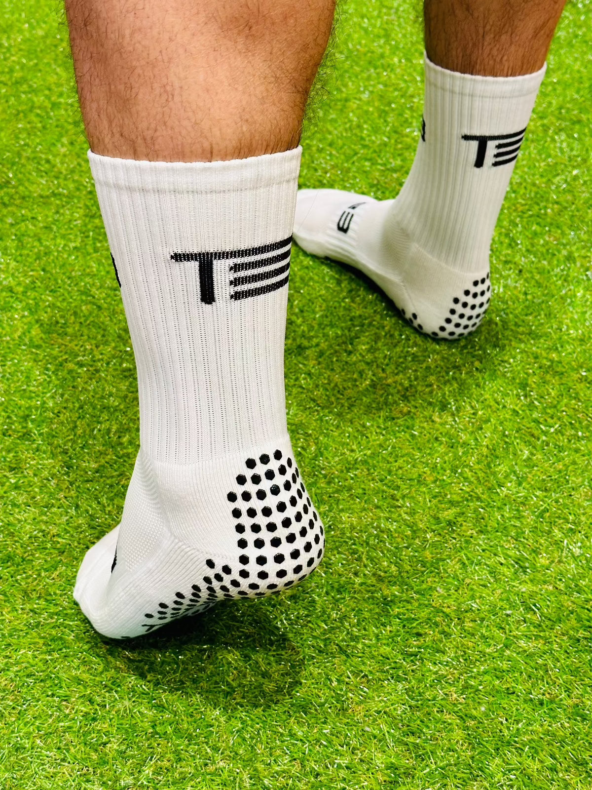 A pair of white high-performance grip socks with black details and the brand 'Tee3' displayed prominently on the side.
